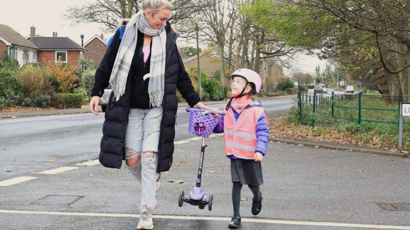 Young girl in hi-vis crossing the road with her mum
