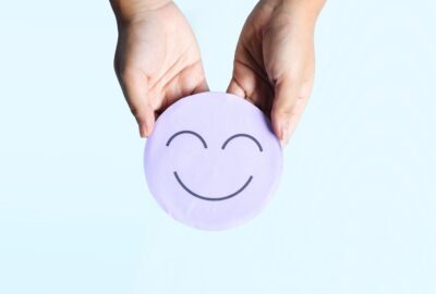 An image that shows a two hands holding a round disk, and the disk has a smiley face on it