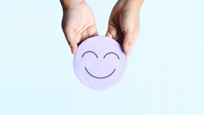 An image that shows a two hands holding a round disk, and the disk has a smiley face on it