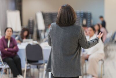A business workshop session, with lead speaker talking to other people in a room