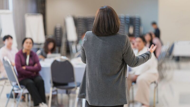 A business workshop session, with lead speaker talking to other people in a room