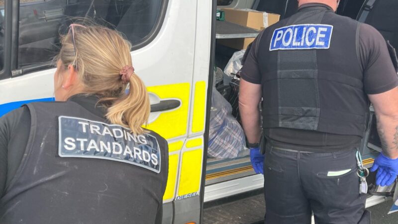 A Trading Standards officer and a Devon and Cornwall Police officer putting counterfeit products into a police van