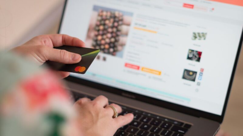A person looking at a website on his laptop, and he is holding his credit card, as if to make a payment
