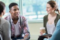 A group of young adults, holding cups of hot drink, chatting, smiling.