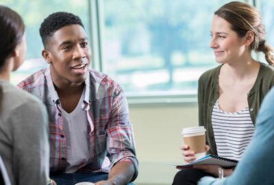 A group of young adults, holding cups of hot drink, chatting, smiling.
