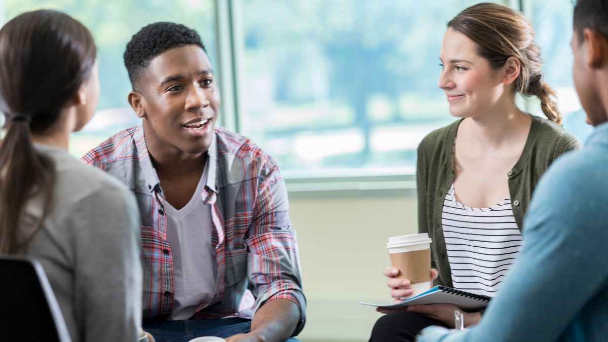 A group of young adults, holding cups of hot drink, chatting, smiling.