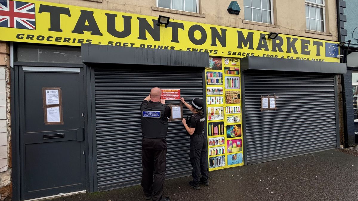 External photo of the shop Taunton Market, with Police and Trading Standards officers putting up a 'closure' notice on the shop's shutters