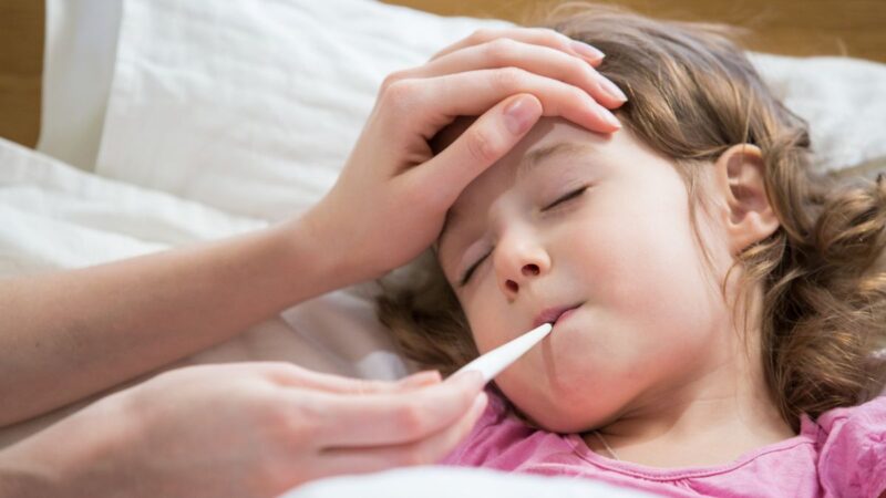 A young child, unwell, lying in bed and her parent is taking her temperature with a thermometer in their mouth