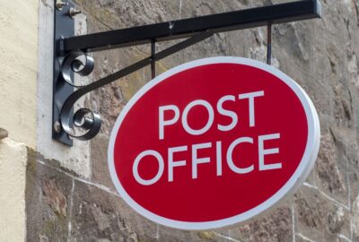 A post office sign hanging on the wall outside a post office
