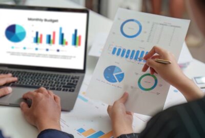 People working at a desk with a laptop and charts, looking at budget figures