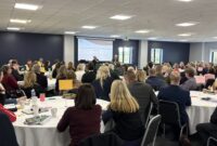 Guests at the conference, all sat around tables and looking toward the front of the conference hall.