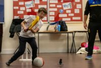 Boy in the classroom playing, (supervised) with a cricket bat and a football, having fun.