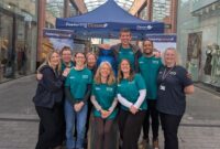 The Promoting Stability Team from Devon County Council's fostering service, stood, celebrating, in front of their Fostering Devon stand, at Princesshay.