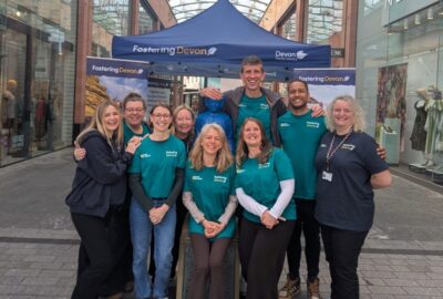 The Promoting Stability Team from Devon County Council's fostering service, stood, celebrating, in front of their Fostering Devon stand, at Princesshay.