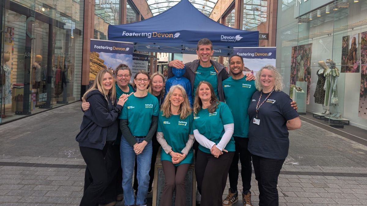The Promoting Stability Team from Devon County Council's fostering service, stood, celebrating, in front of their Fostering Devon stand, at Princesshay.