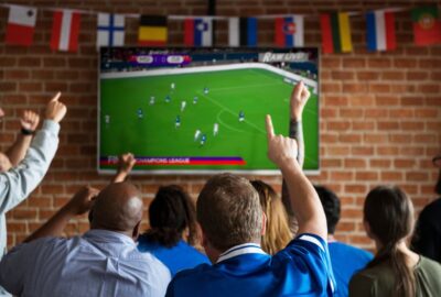 Adults watching a big screen with the football on. Men waving their arms