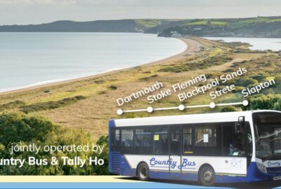 A bus, with Country Bus logo on the side of the bus, on a road, with Slapton in the background