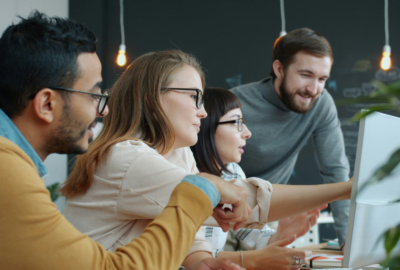 Group of young professionals looking at a computer screen together in a workplace environment.