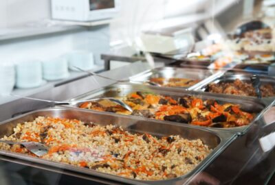School dinners, in large catering trays, containing pasta and other foods.