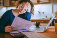A lady, holding her head in her hands, looking at a household bill.