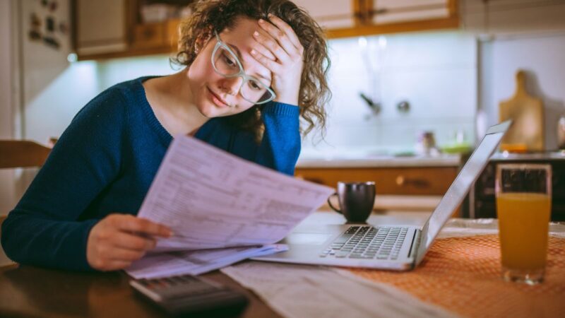 A lady, holding her head in her hands, looking at a household bill.