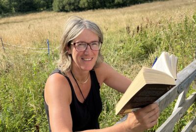Author Vanessa de Haan smiling while reading a book outdoors in the Blackdown Hills
