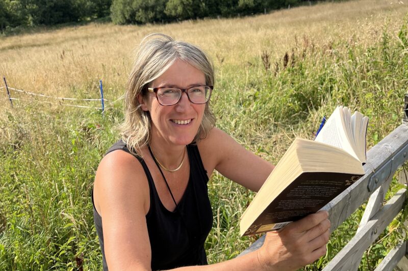 Author Vanessa de Haan smiling while reading a book outdoors in the Blackdown Hills