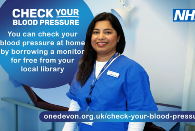 NHS promotional graphic showing a healthcare worker standing in a clinical setting. Text reads: “Check your blood pressure. You can check your blood pressure at home by borrowing a monitor for free from your local library.” Includes the One Devon website for more information.
