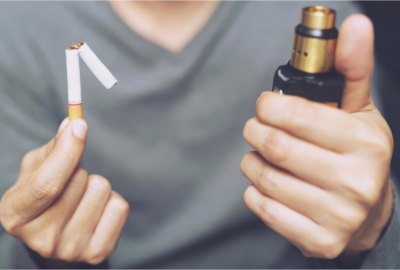Close up of a person holding a snapped cigarette in one hand and a vaping device in the other