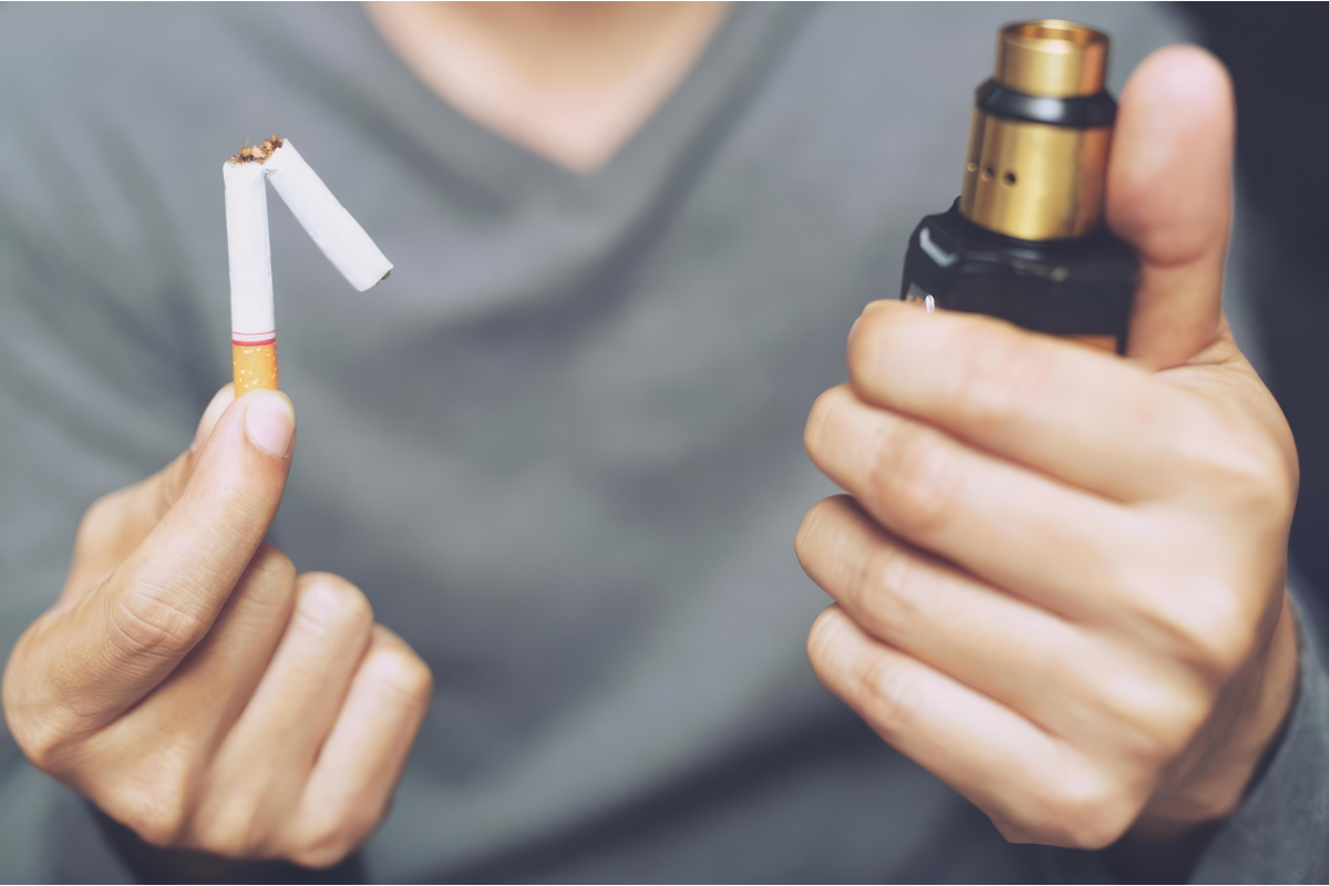 Close up of a person holding a snapped cigarette in one hand and a vaping device in the other