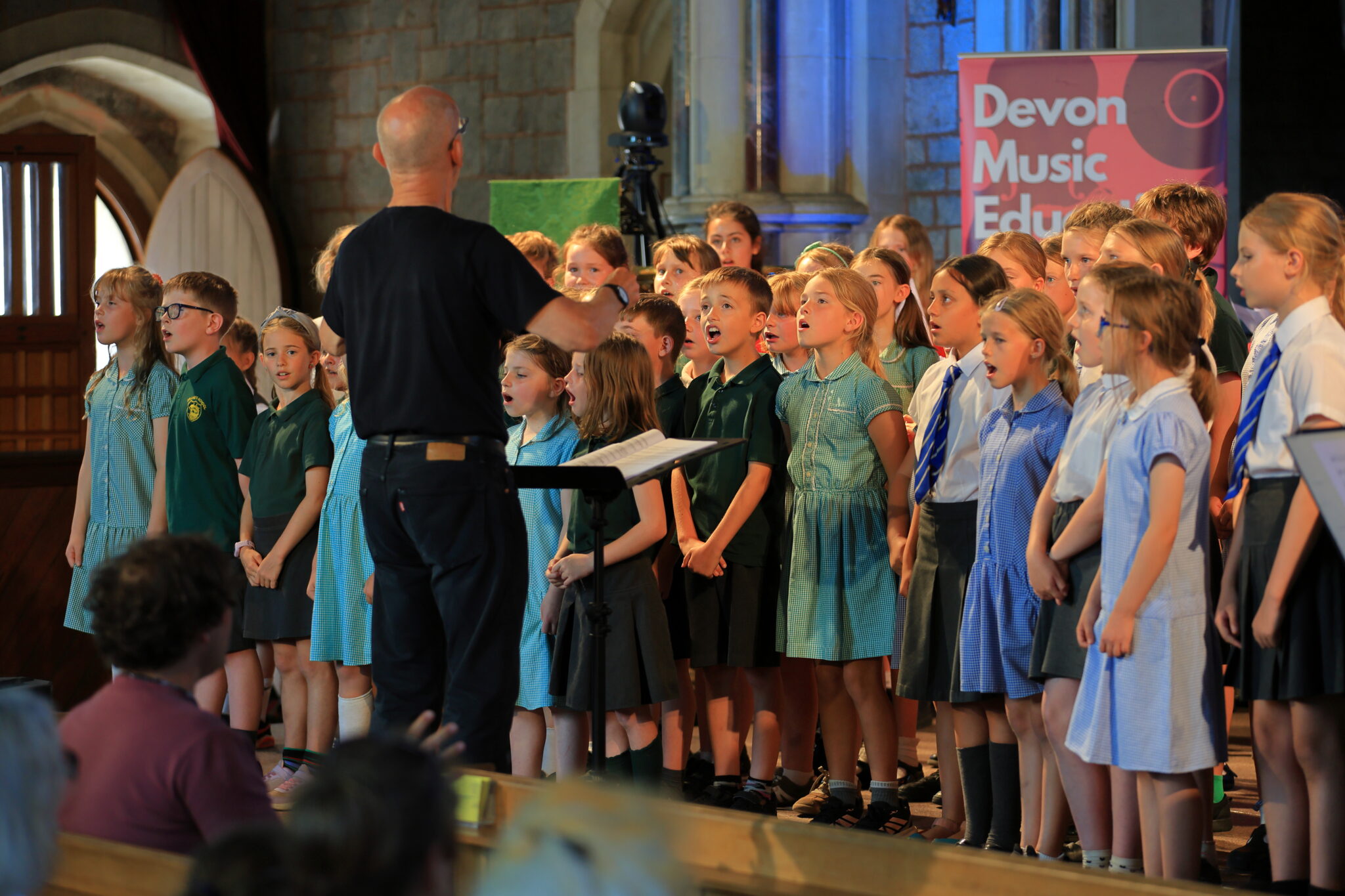 Children singing in a choir with a conductor.