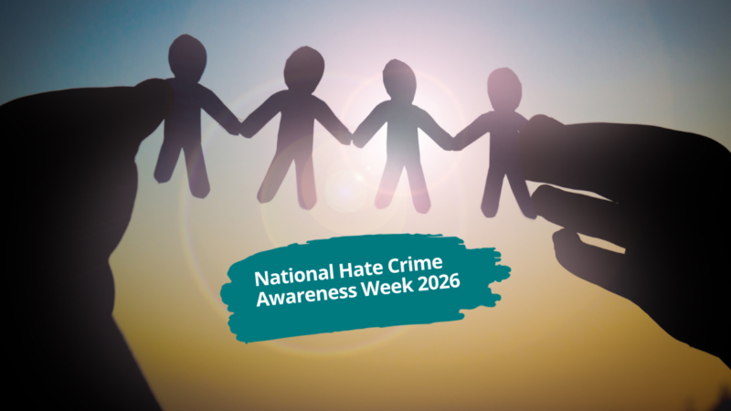 Silhouetted hands hold a chain of four paper figures against a sunlit background, with the text: “National Hate Crime Awareness Week 2026”.