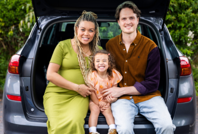 Photo depicting a smiling adoptive family sitting in the boot of a car