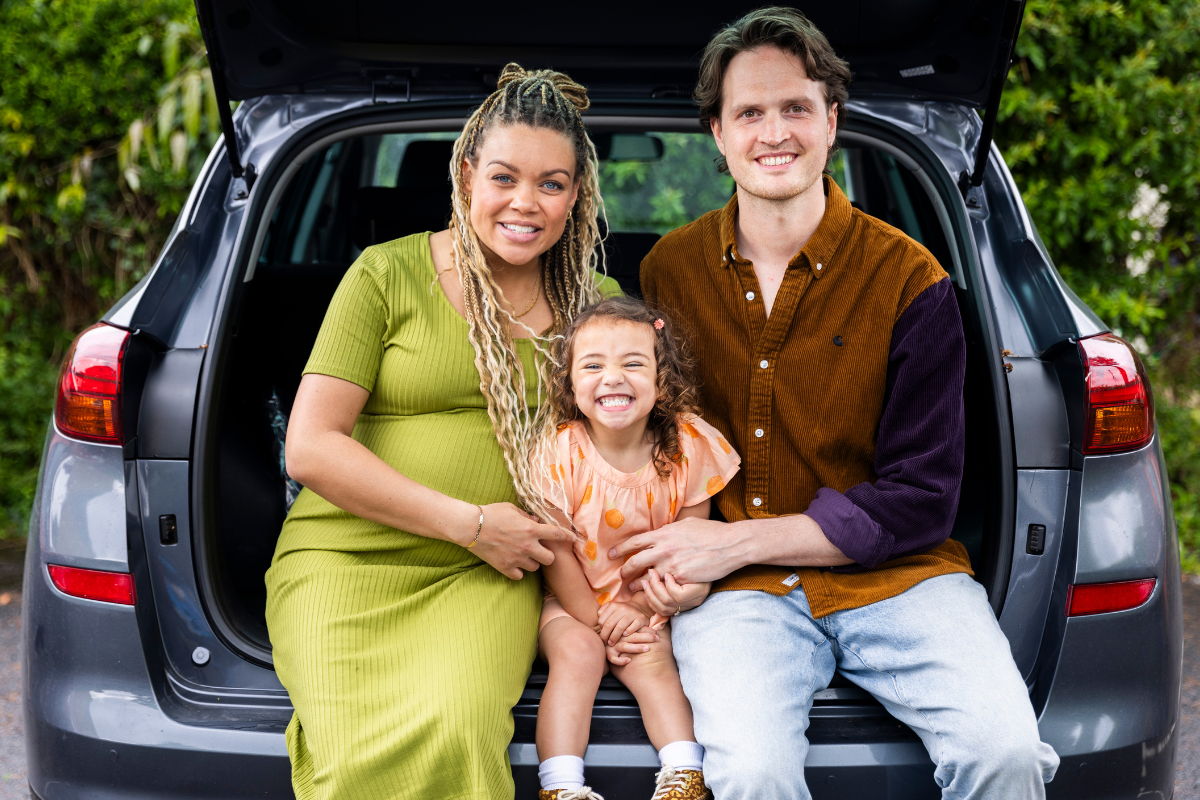 Photo depicting a smiling adoptive family sitting in the boot of a car