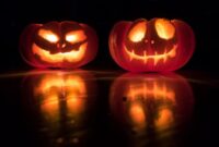 Two glowing carved Halloween pumpkins against a dark background.
