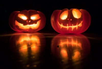 Two glowing carved Halloween pumpkins against a dark background.