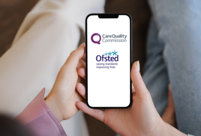 Two people sitting on a sofa looking at a smartphone that has the CQC and Ofsted logos on it.
