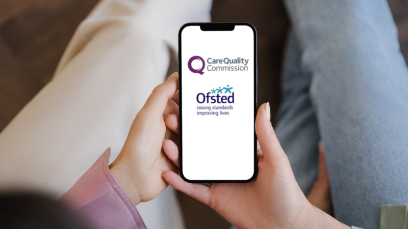 Two people sitting on a sofa looking at a smartphone that has the CQC and Ofsted logos on it.
