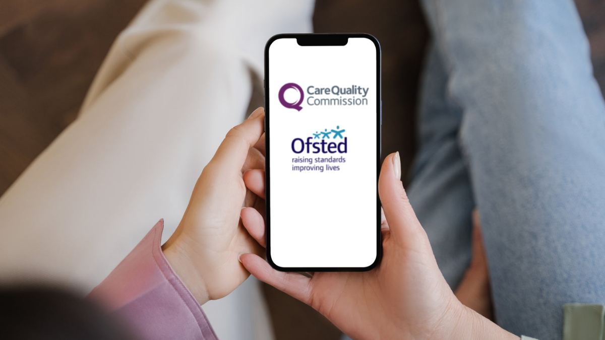 Two people sitting on a sofa looking at a smartphone that has the CQC and Ofsted logos on it.