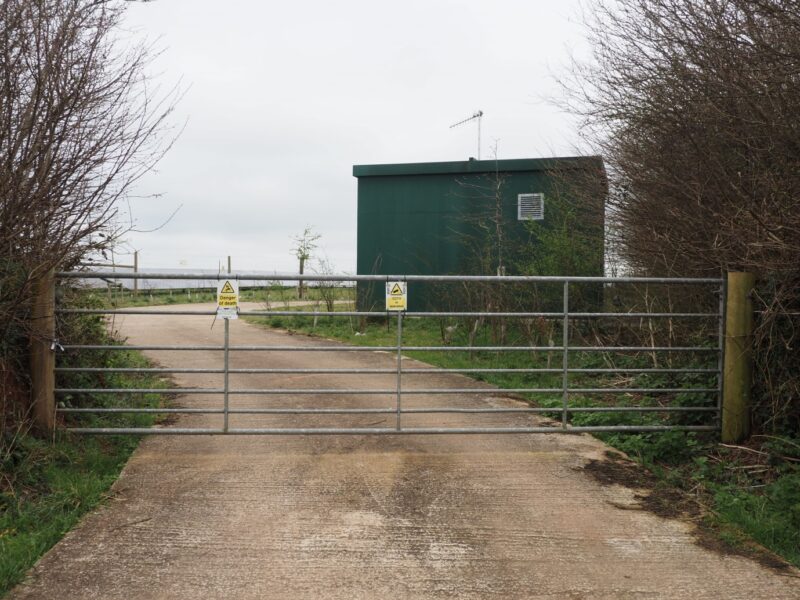 An auxiliary building for a PV development behind a gate and with new trees planted to screen it.