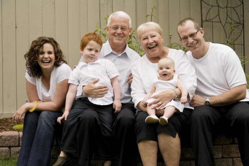 Generations of a Devon family smiling and laughing together, sat on bench outside.