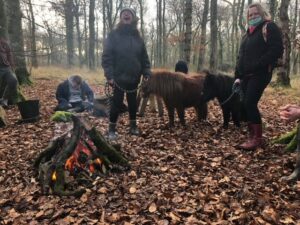 A group of people with ponies in the woods.