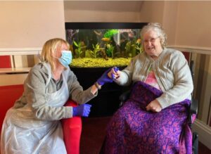 Two women in care home sitting in chairs and holding hands.