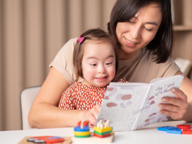 cute child with down syndrome girl with mum and book at home