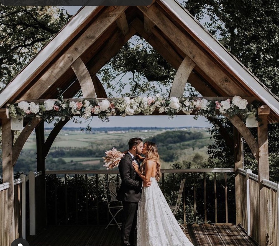 A bride and groom kissing in a wooden structure decorated with flowers