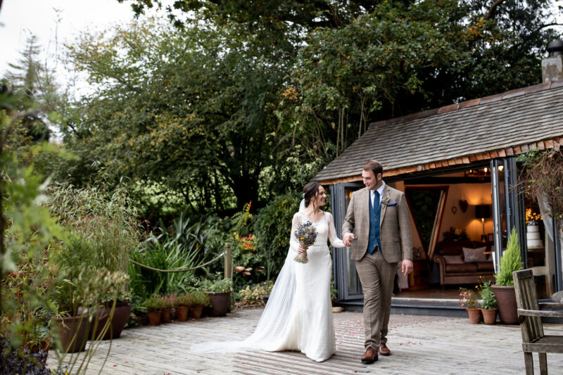 A bride and groom standing on a wooden decked area outside a wooden summer house
