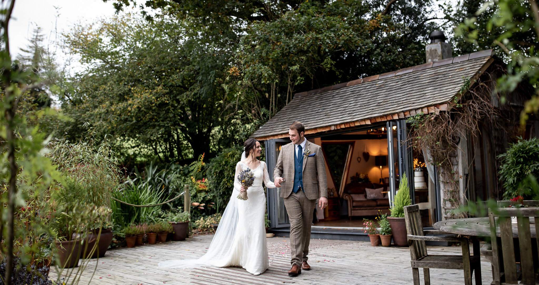 A bride and groom standing on a wooden decked area outside a wooden summer house