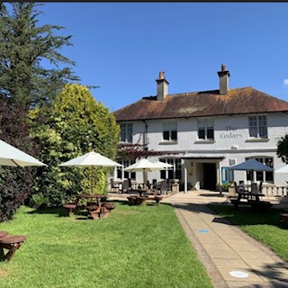 A white building with a thatched roof and garden area with tables and parasols.