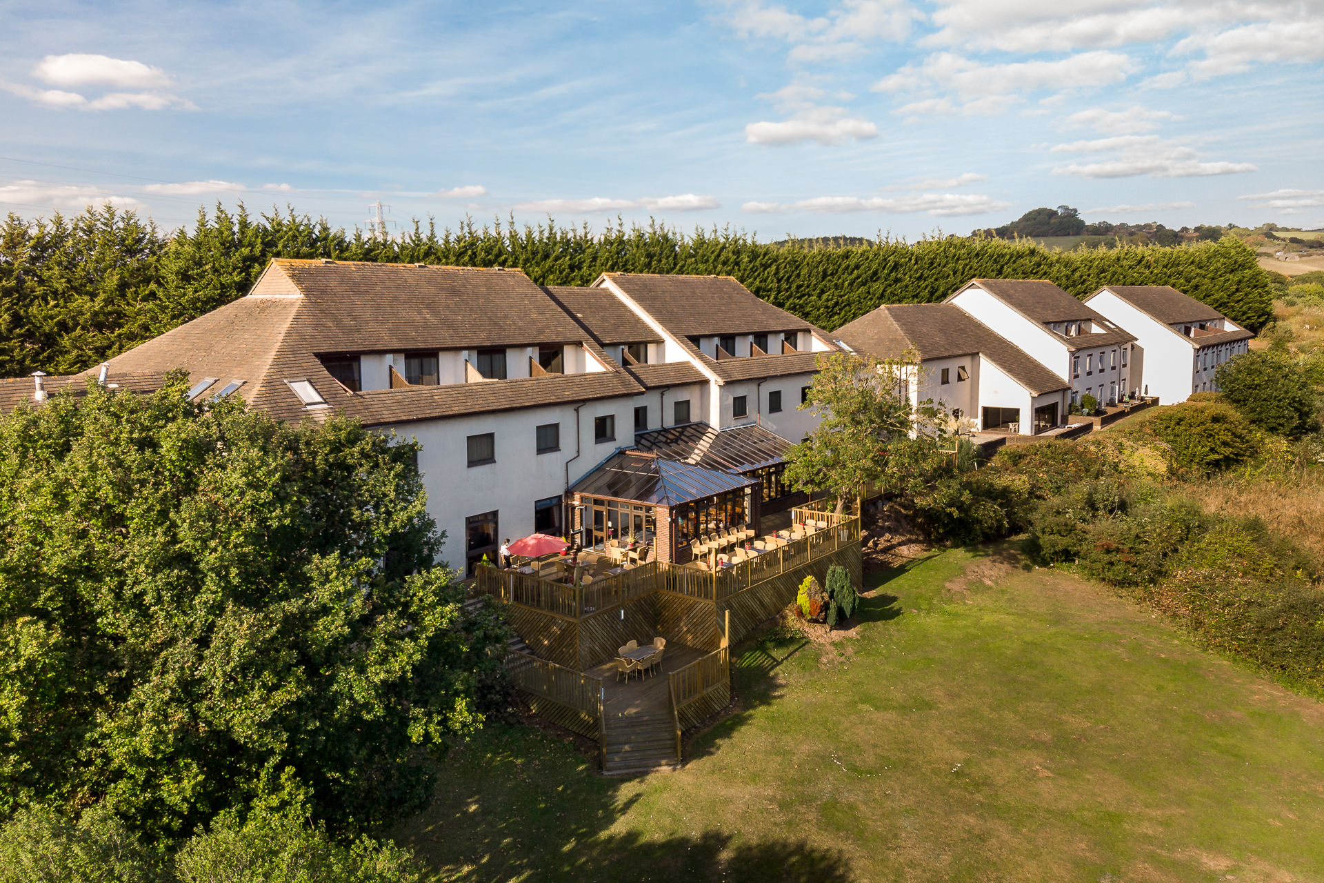 A rear view of a white building, showing a conservatory and decking area, with lawn beyond.