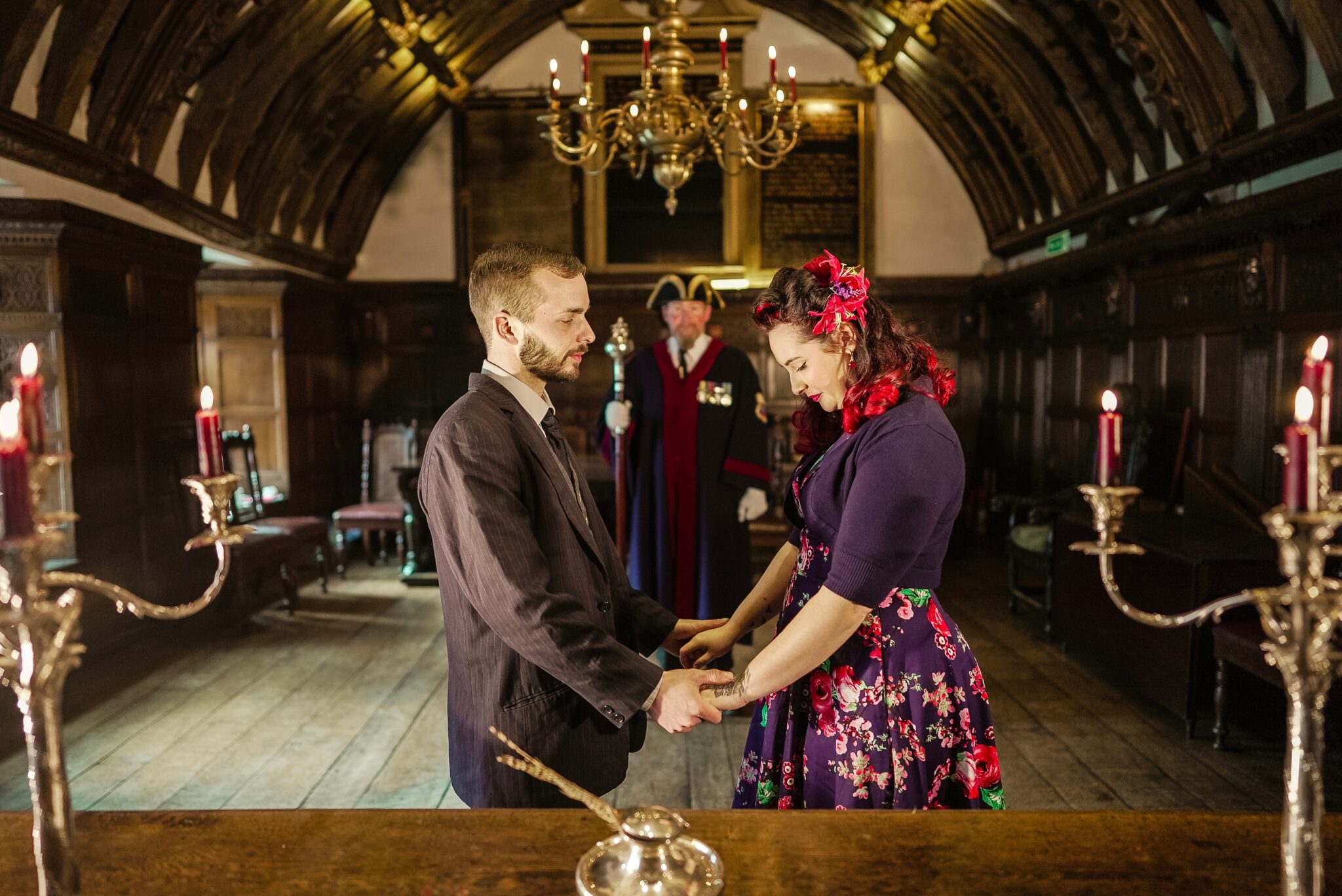 A couple facing each other, holding hands in the wooden panelled hall.